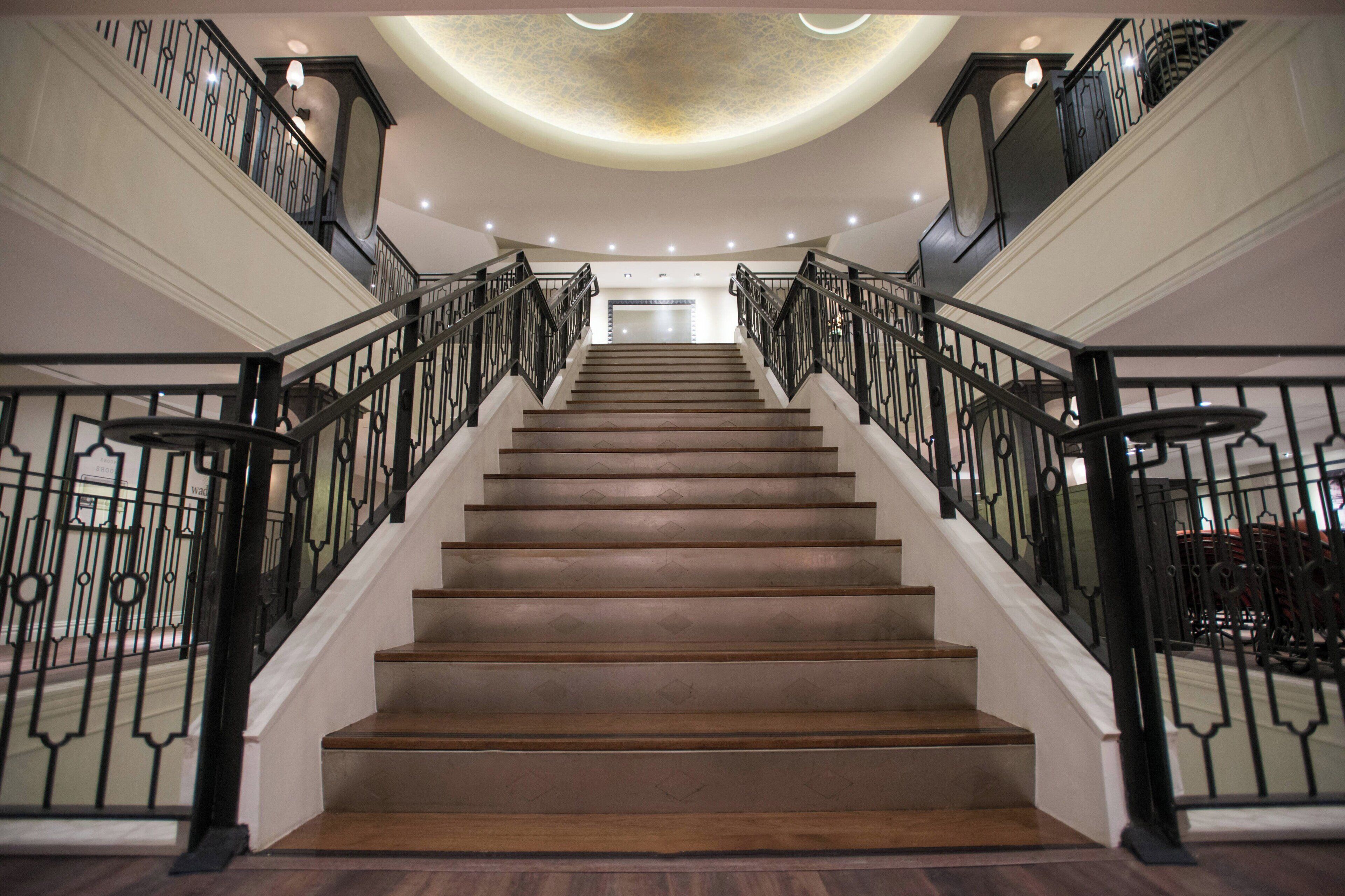 Eine prächtige Treppe mit aufwendiger schwarzer Geländer und glänzendem Holzboden, die zu einer Empore mit dekorativer Decke führt.