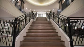 A grand staircase with ornate black railings and a polished wooden finish, leading to a landing with a decorative ceiling.