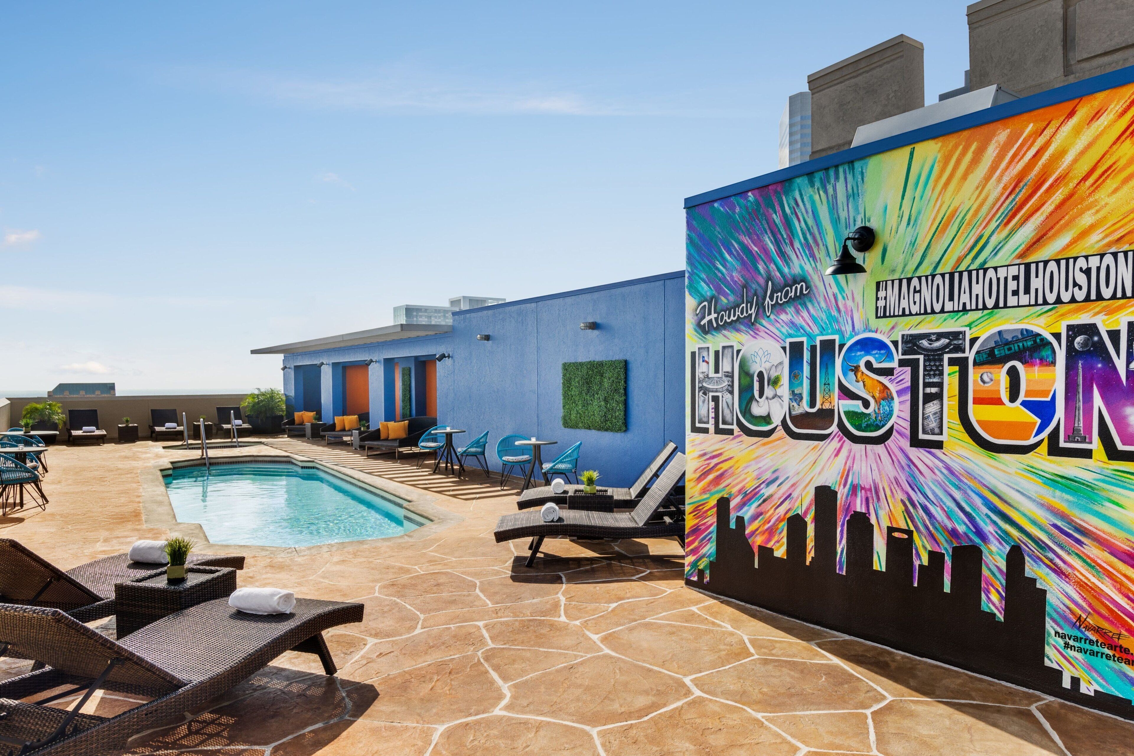 A hotel pool area with lounge chairs, a pool, and a colorful mural with the hotel name.