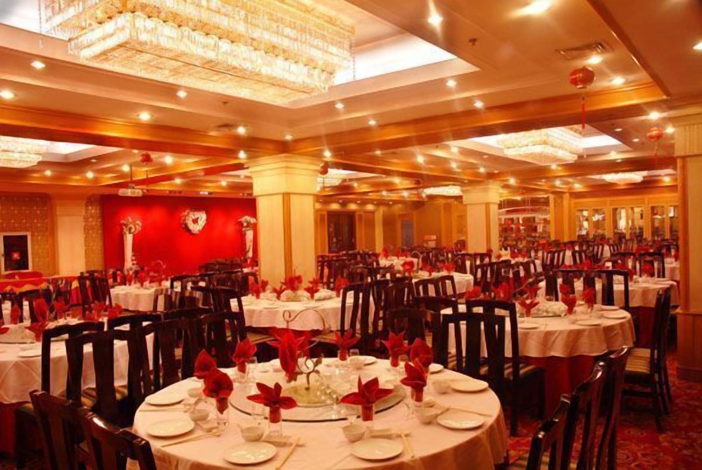 Ein Festsaal mit runden Tischen, gedeckt für ein Essen, mit roten floralen Tischdekorationen und weißen Tischdecken.
