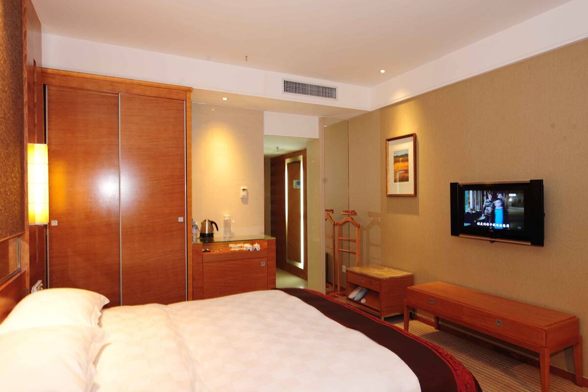 Habitación de hotel con una cama grande, un armario de madera, un escritorio pequeño, televisor y espejo.