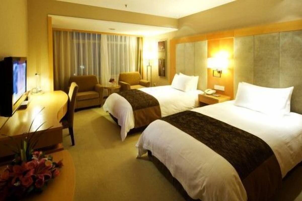 Habitación de hotel con dos camas, un escritorio, una silla y un televisor.