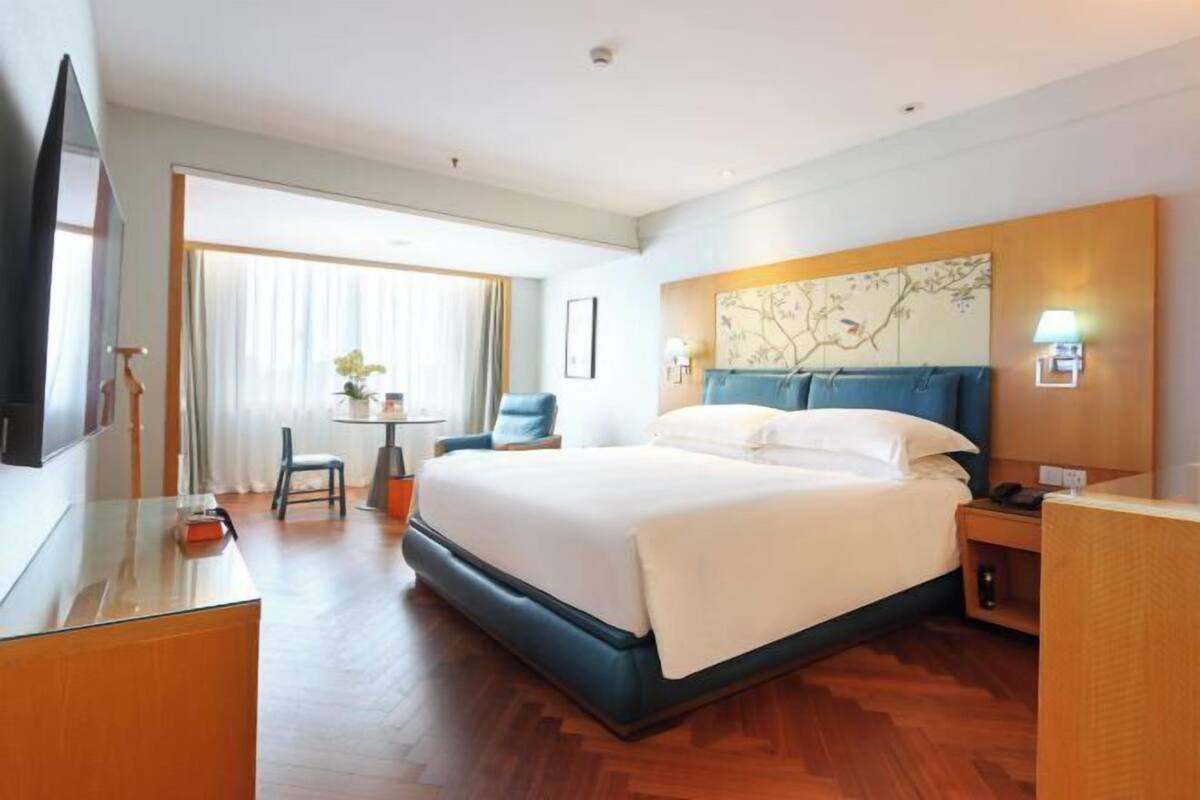 Habitación de hotel con cama, escritorio, silla, televisión y ventana con cortinas.