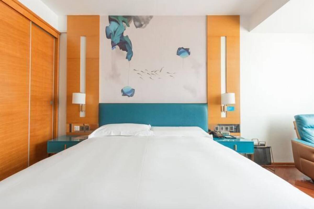 Habitación de hotel con una cama grande, cabecera azul, dos mesitas de noche con lámparas, un escritorio y una silla.