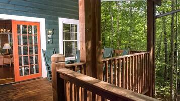 A wooden deck with a railing, a door with a red frame, and a view of a forested area.