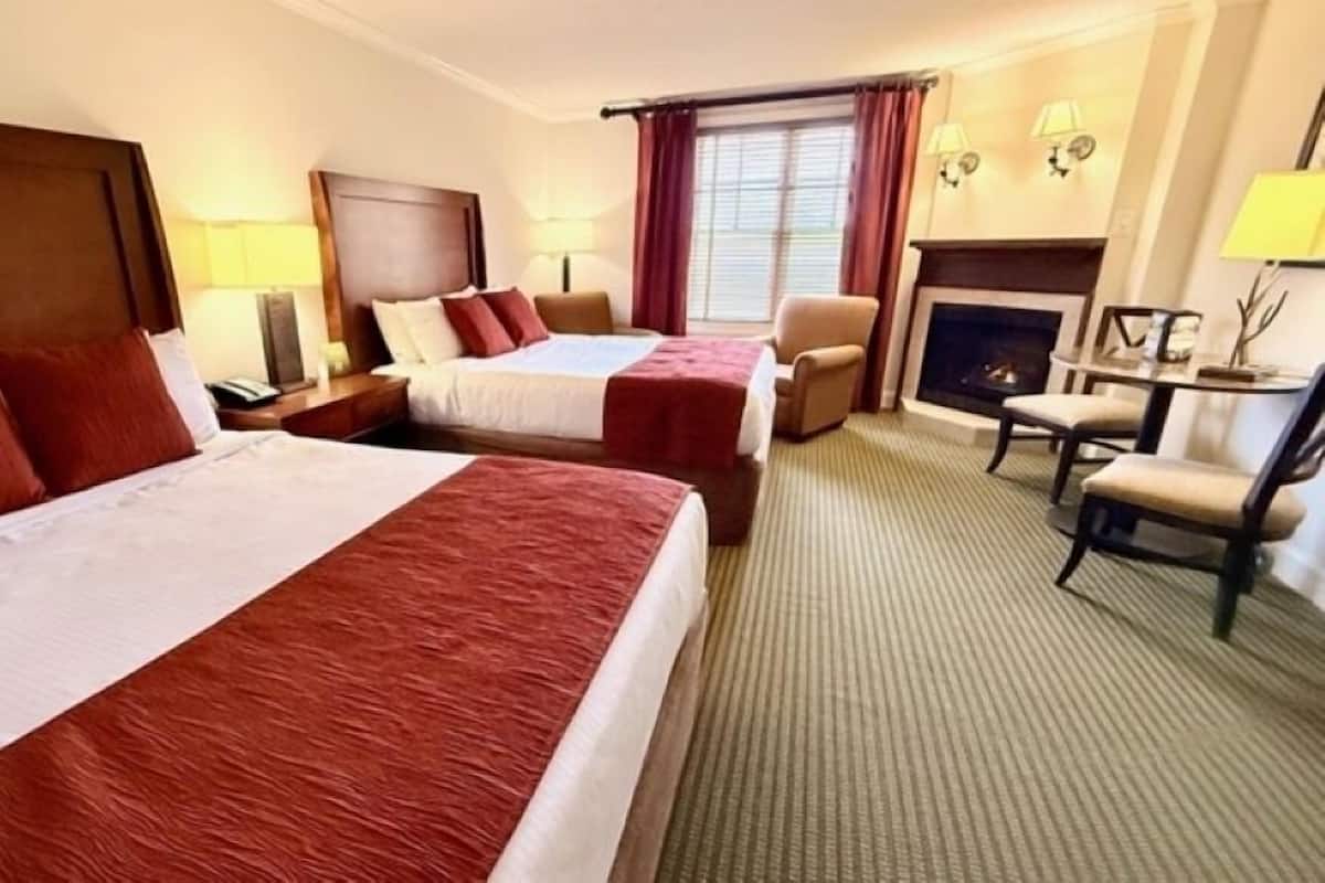 A hotel room with two beds, a sofa, a dining table, and a fireplace.