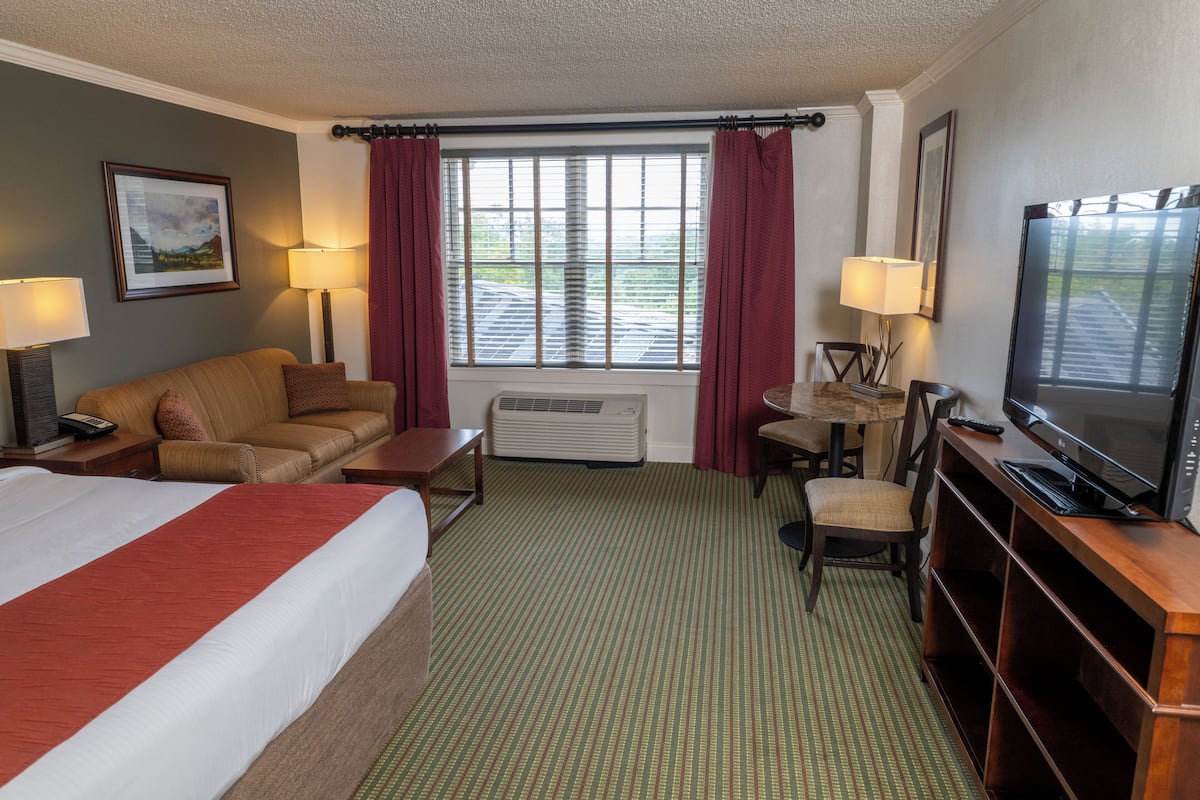 A hotel room with a large bed, a sofa, a desk, a television, and a window with curtains.