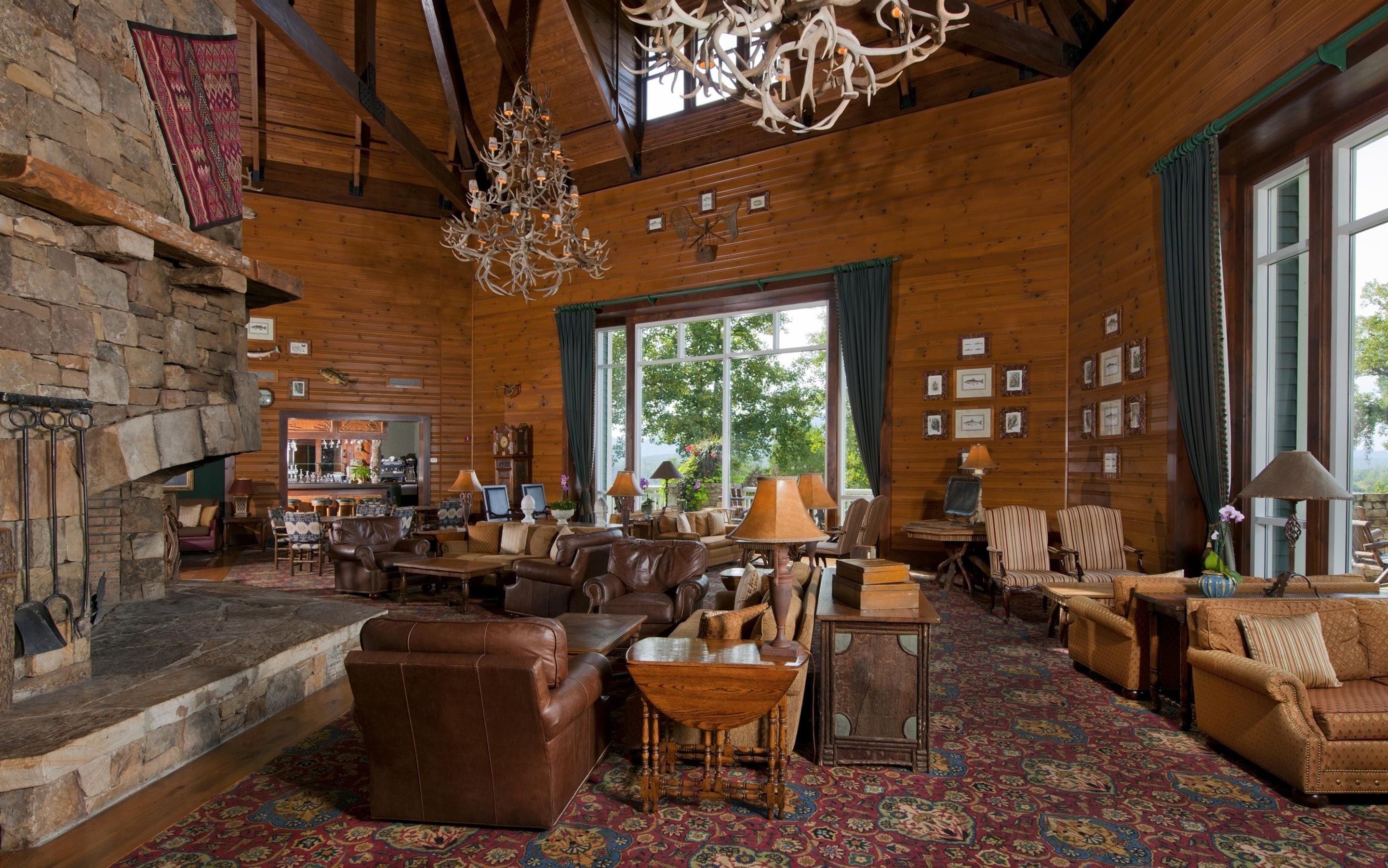 A cozy lodge interior with a stone fireplace, leather furniture, and a large window offering a view of the outdoors.