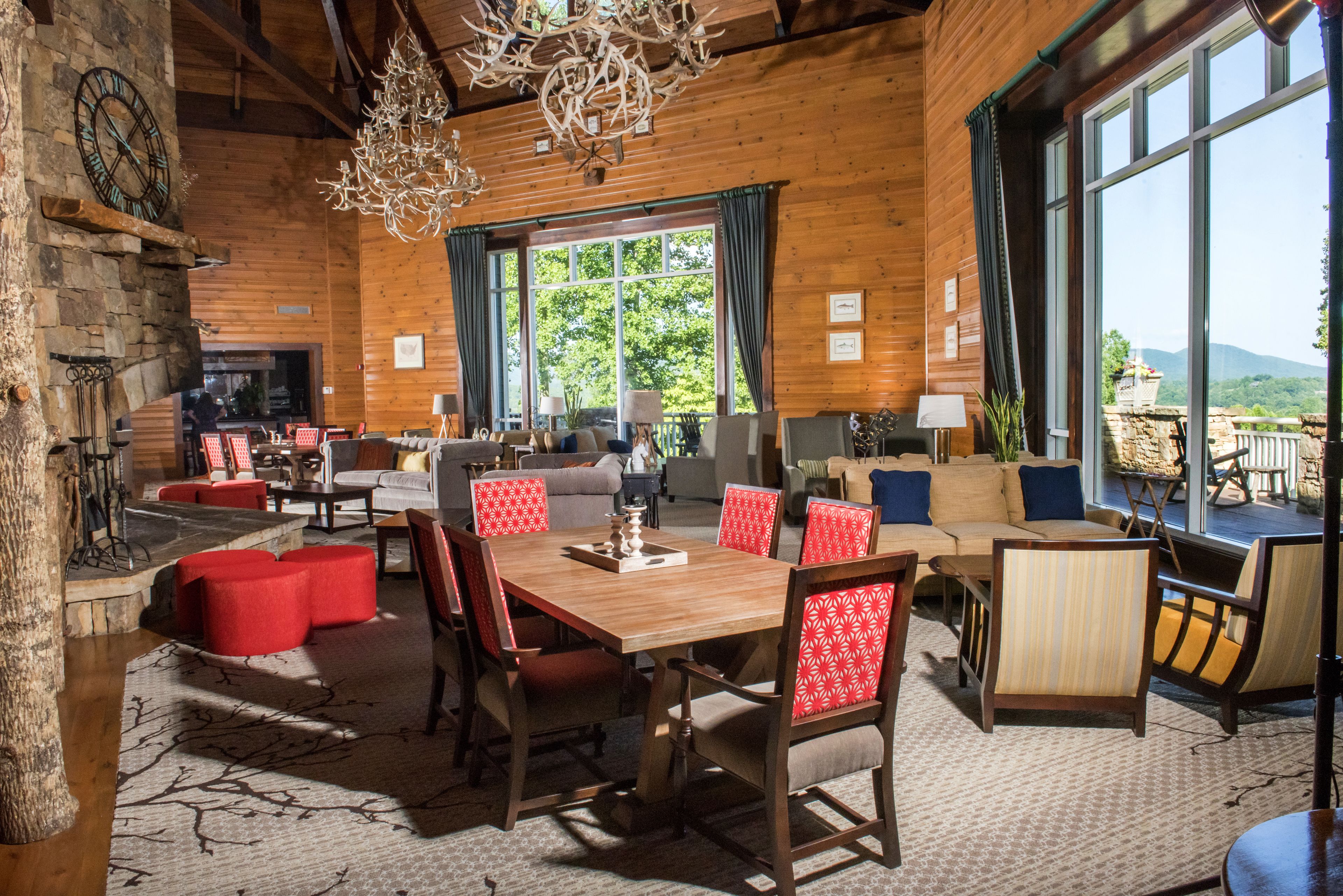 A spacious lodge with a wooden interior, a dining area with red upholstered chairs, and large windows offering a view of the outdoors.
