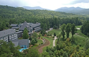 Ein großes Hotel mit mehreren Gebäuden, einem Schwimmbad und einem Golfplatz, umgeben von dichtem Wald und Bergen.