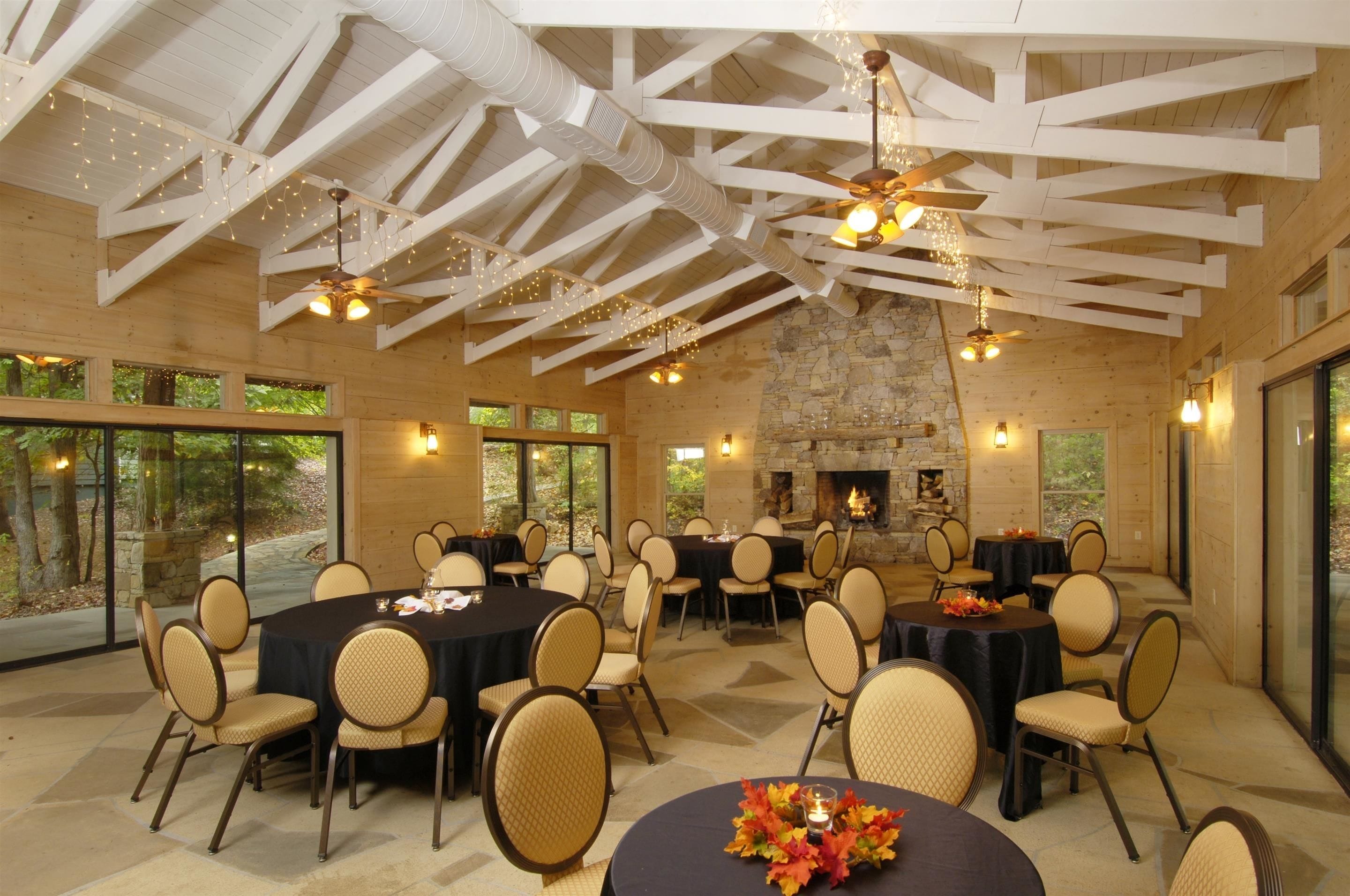 A spacious indoor dining area with high ceilings, stone fireplace, and large windows.