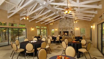 A spacious indoor dining area with high ceilings, stone fireplace, and large windows.