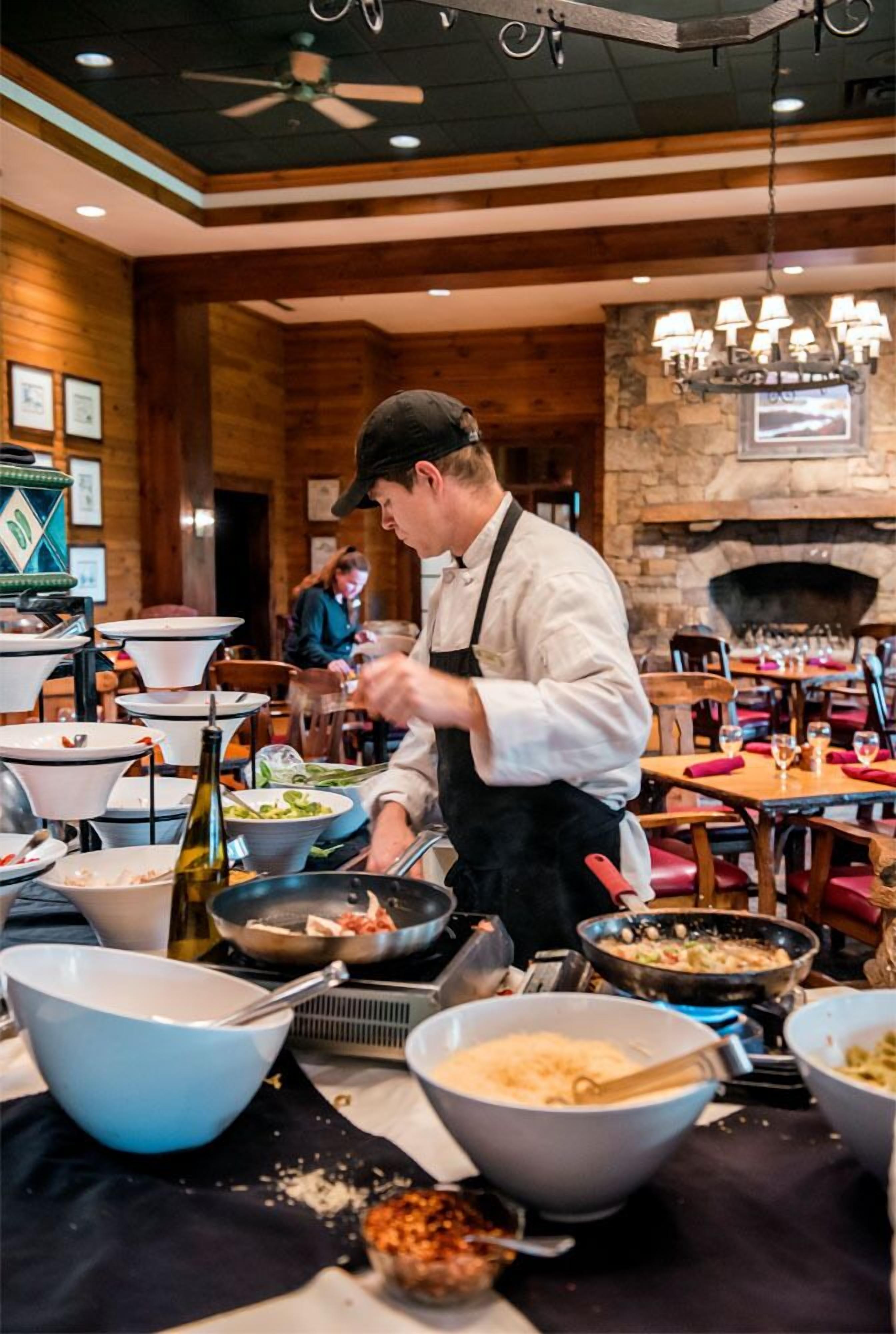 A chef preparing food in a restaurant with wooden walls and a stone fireplace.