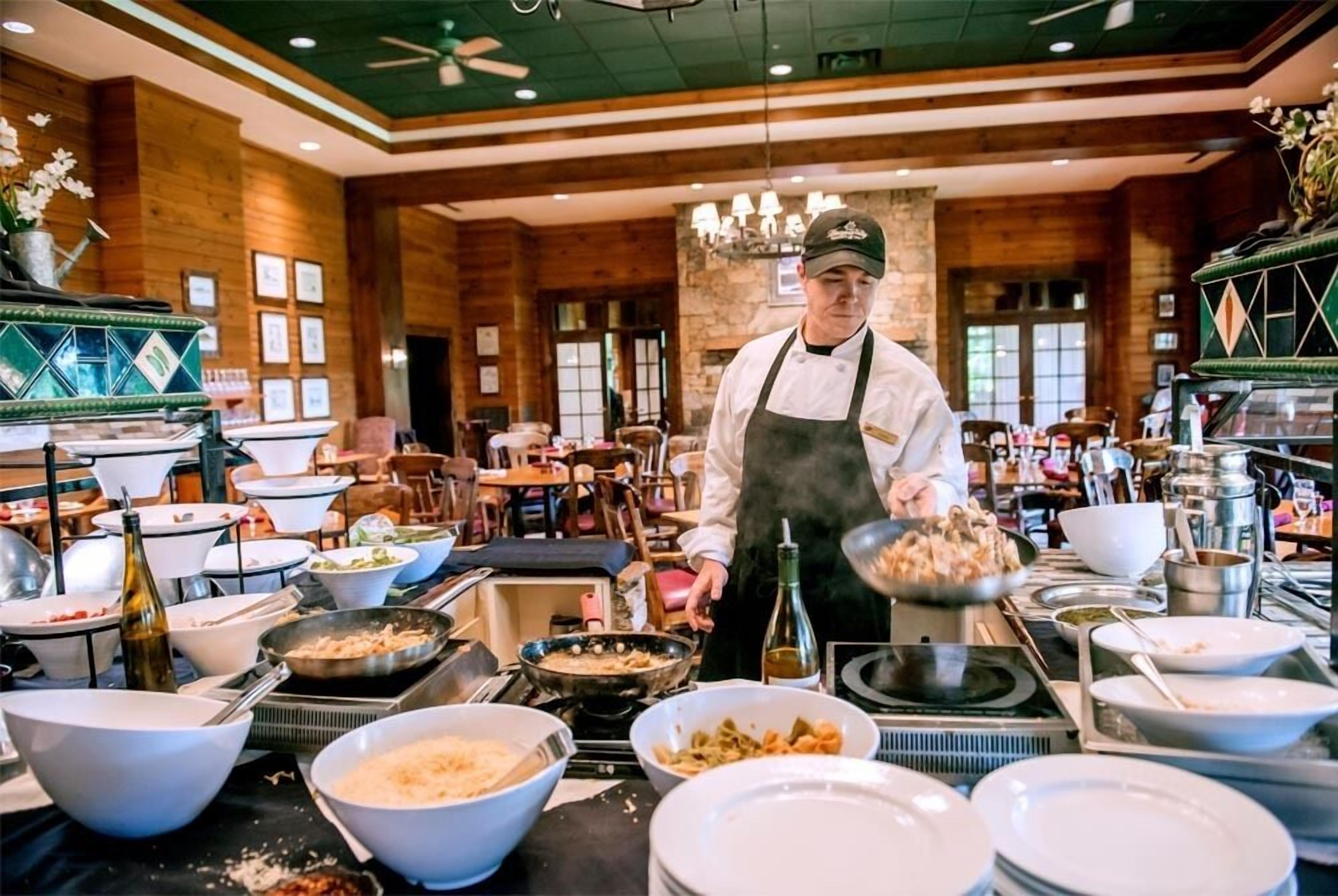 A chef preparing food in a kitchen with wooden walls and a stone fireplace.