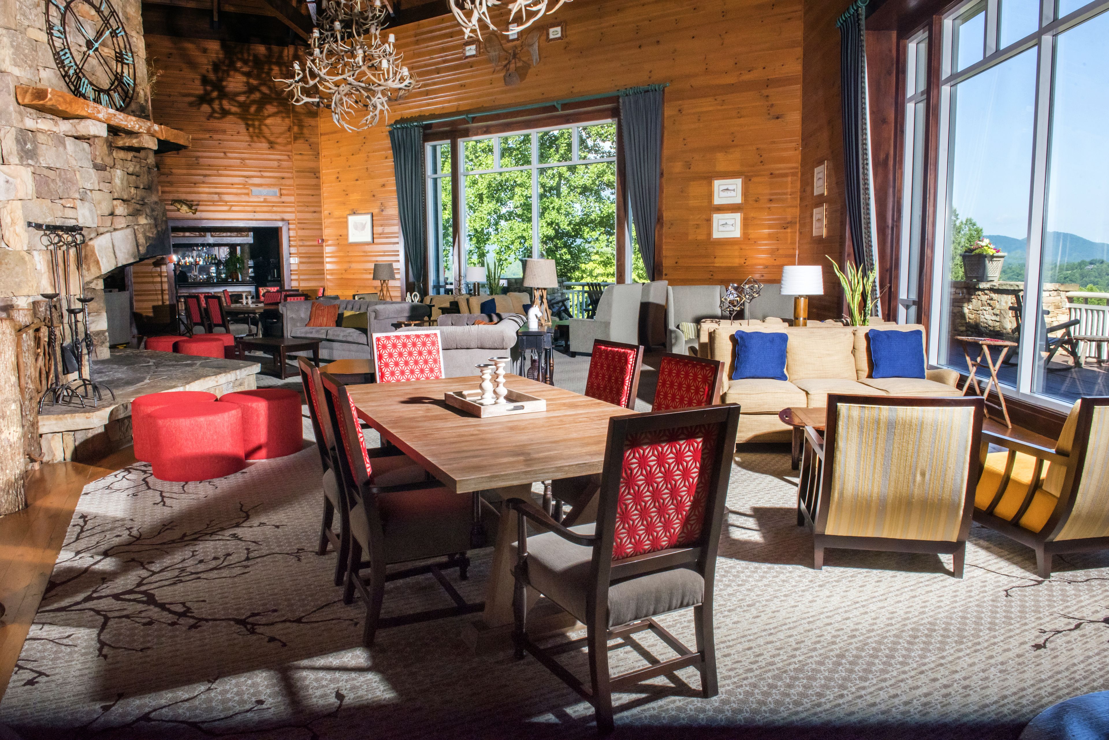 L’intérieur d’un chalet confortable, avec des murs en rondins de bois, une cheminée en pierre, une table à manger en bois et une grande fenêtre donnant sur le paysage extérieur.