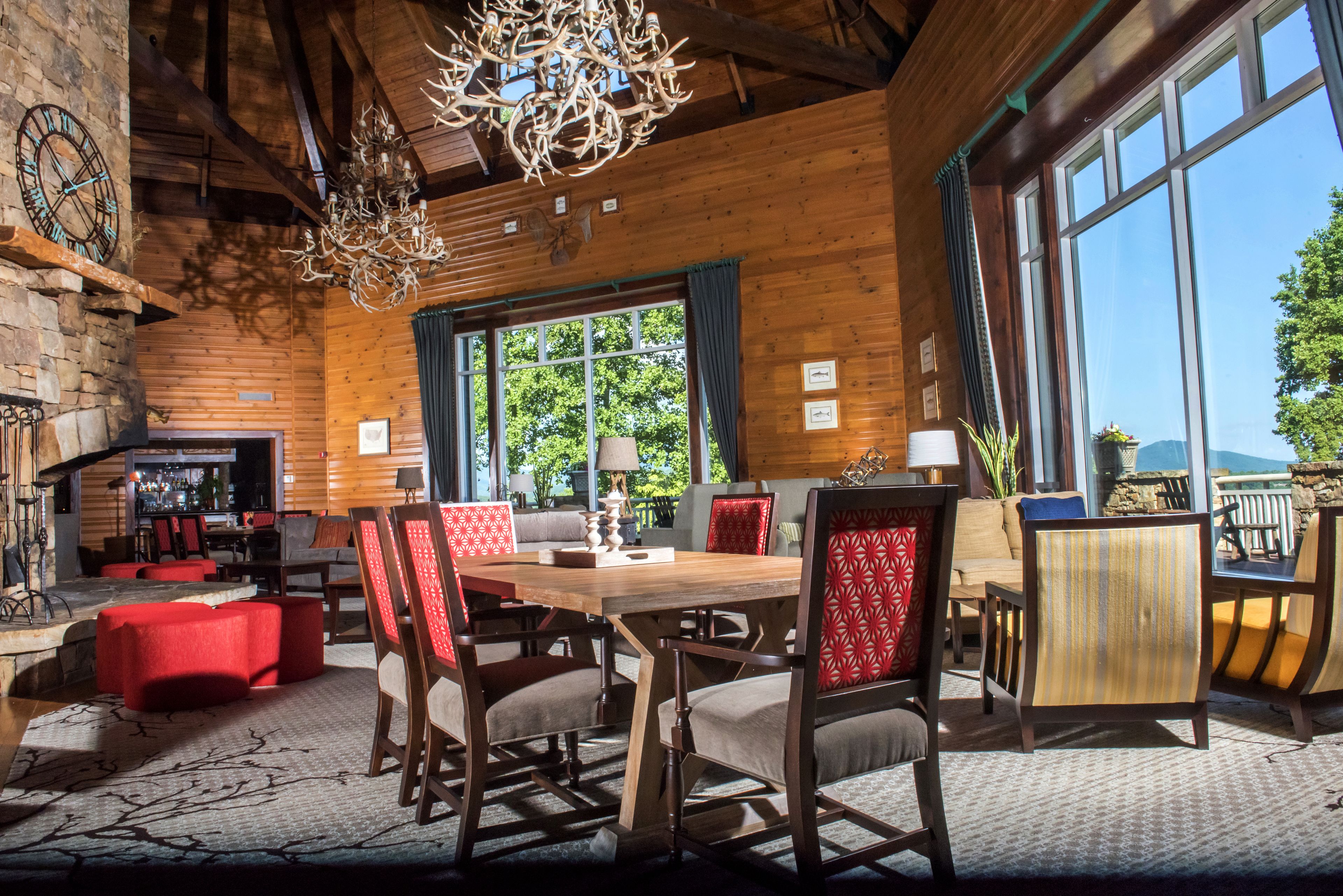 Un interior rústico de madera con un comedor, sillas tapizadas en rojo y un amplio ventanal con vistas a la vegetación.