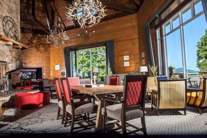 Un interior rústico de madera con un comedor, sillas tapizadas en rojo y un amplio ventanal con vistas a la vegetación.