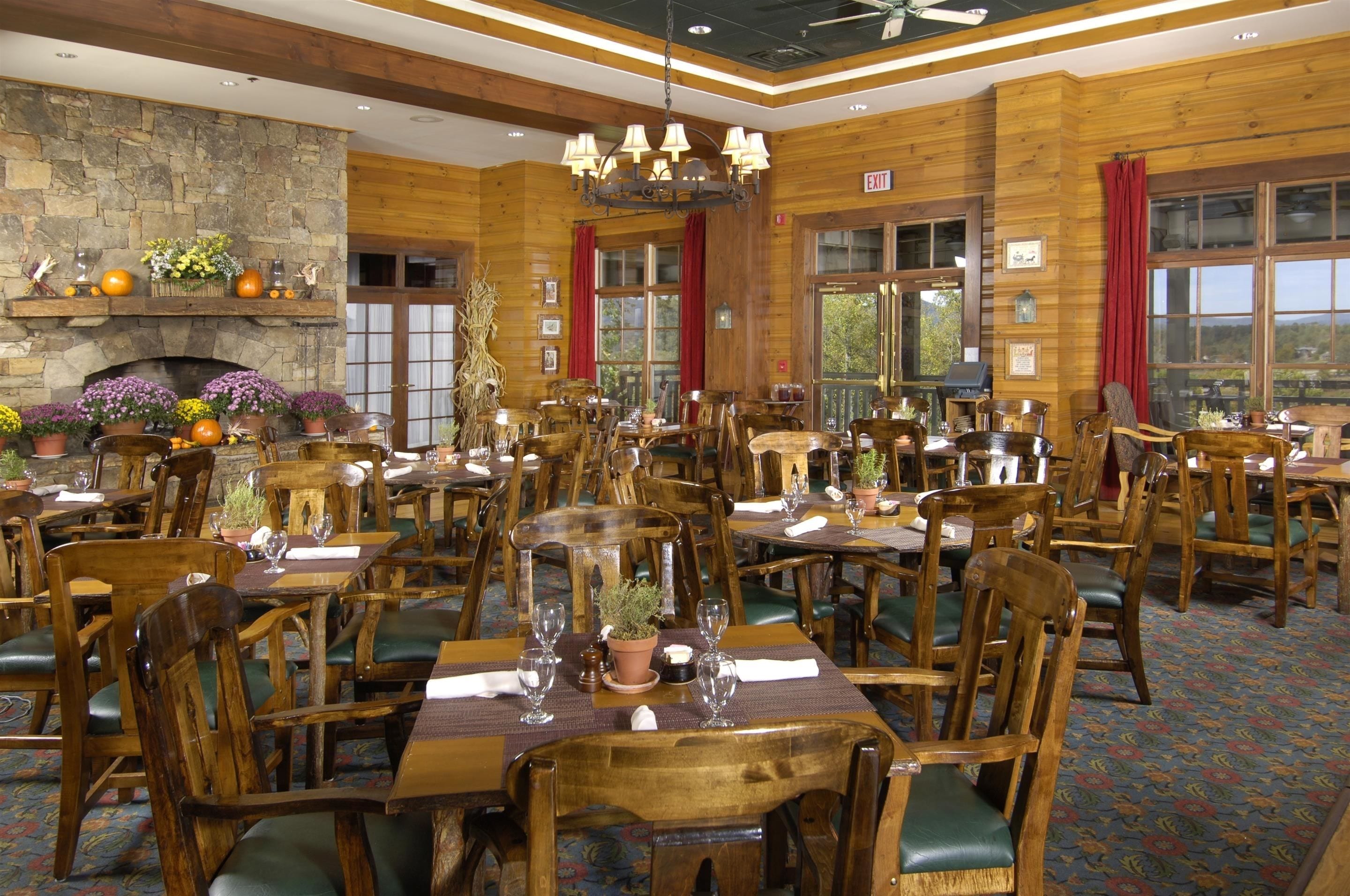 A dining area with wooden tables and chairs, a stone fireplace, and large windows.
