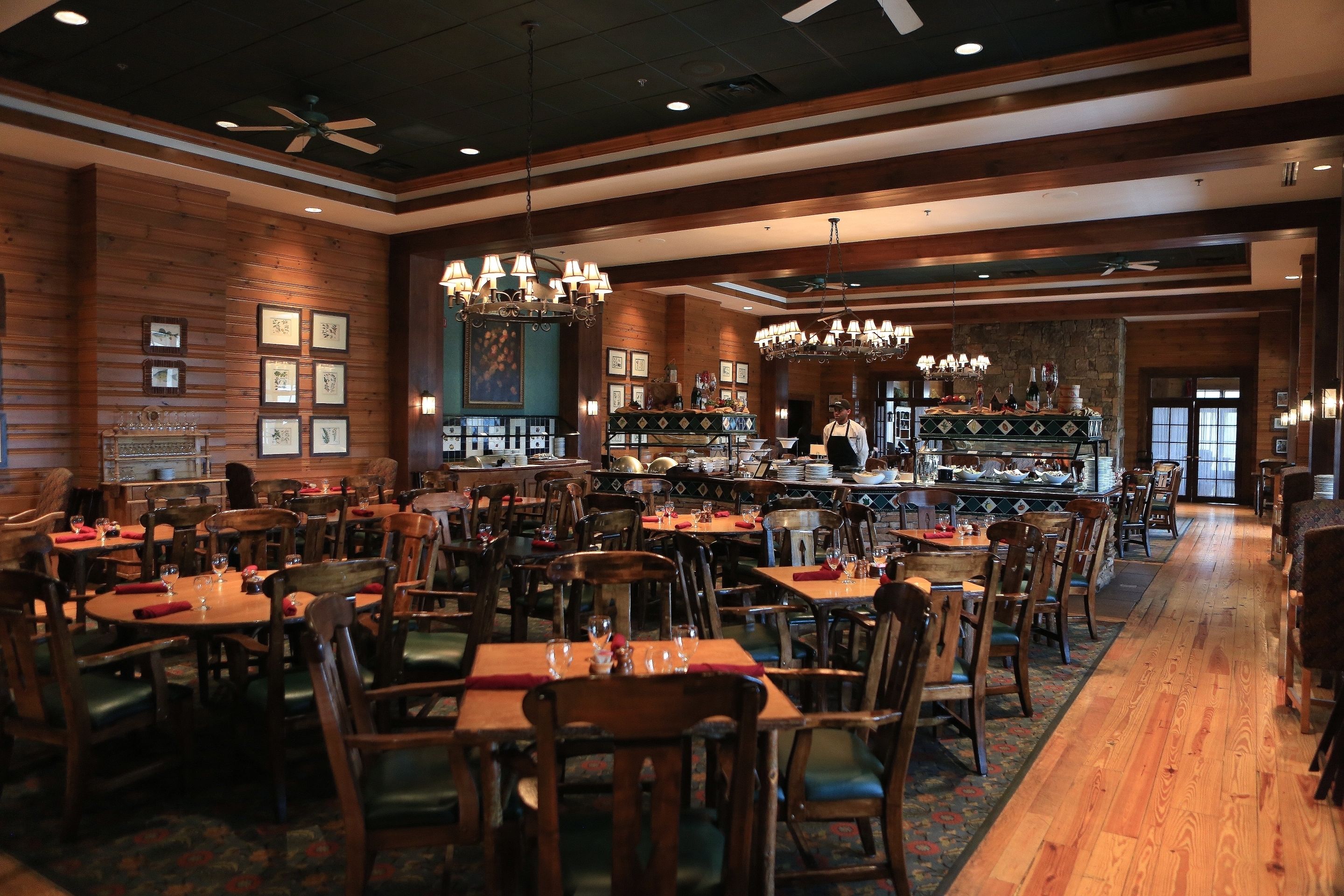 A restaurant with wooden walls, chandeliers, and a bar area.