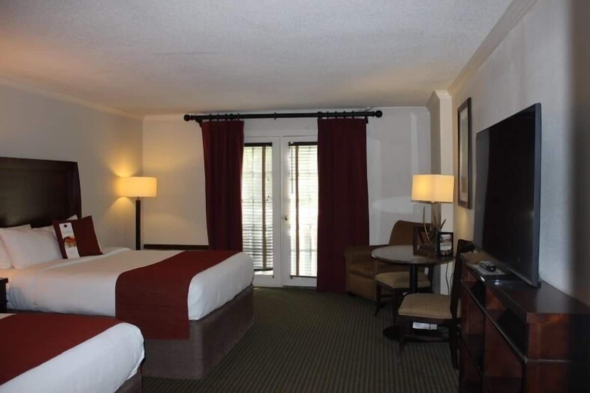 A hotel room with two beds, a desk with a chair, a television, and a window with curtains.