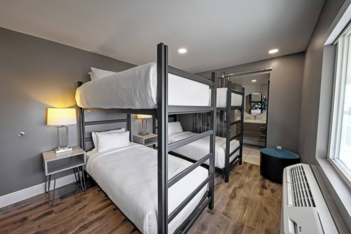 A bunk bed room with a desk, lamp, and a view of the city.
