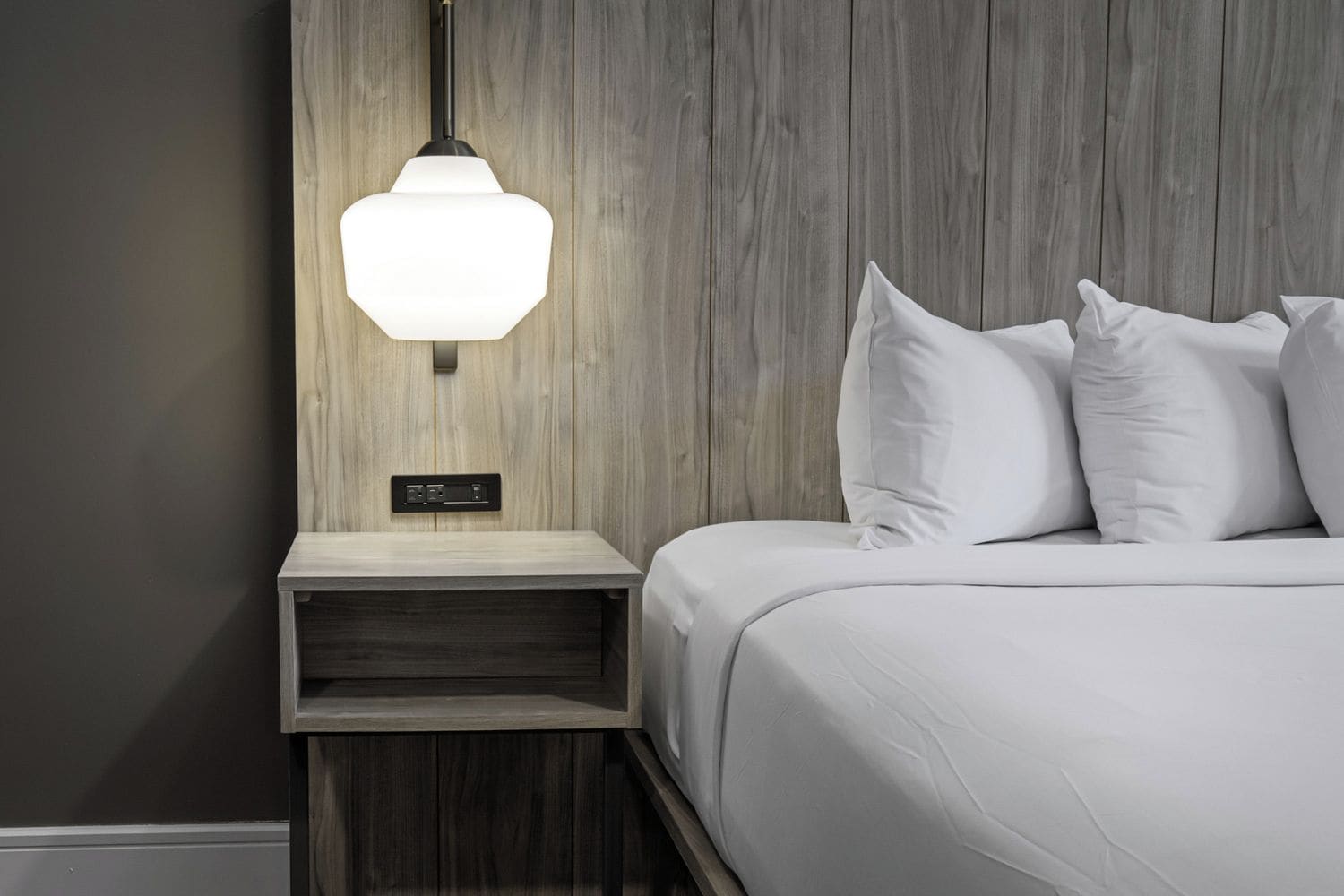 A bedroom with a bed, white pillows, a bedside table, and a wall-mounted lamp.