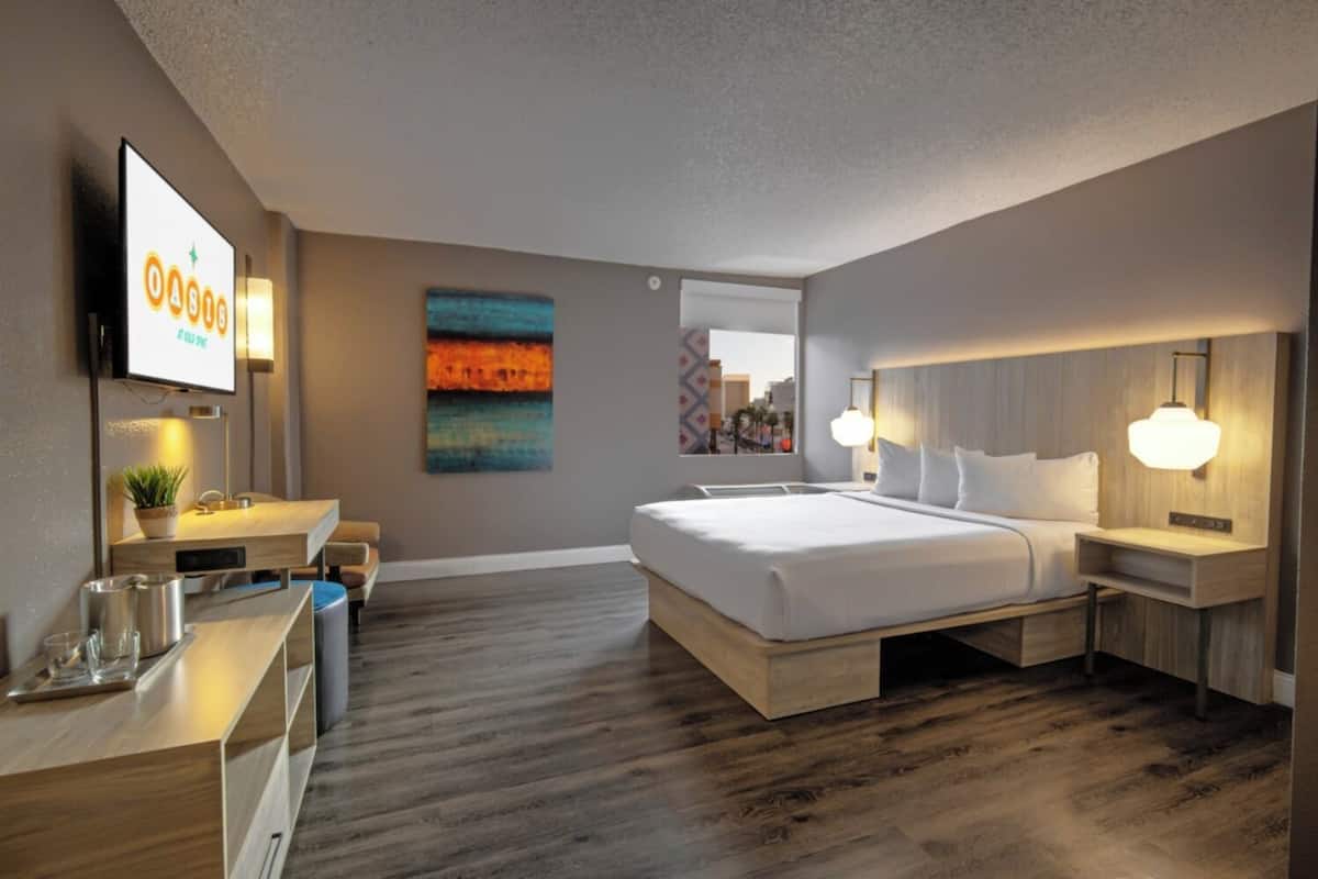 A modern hotel room with a large bed, bedside tables, a desk, and a TV.