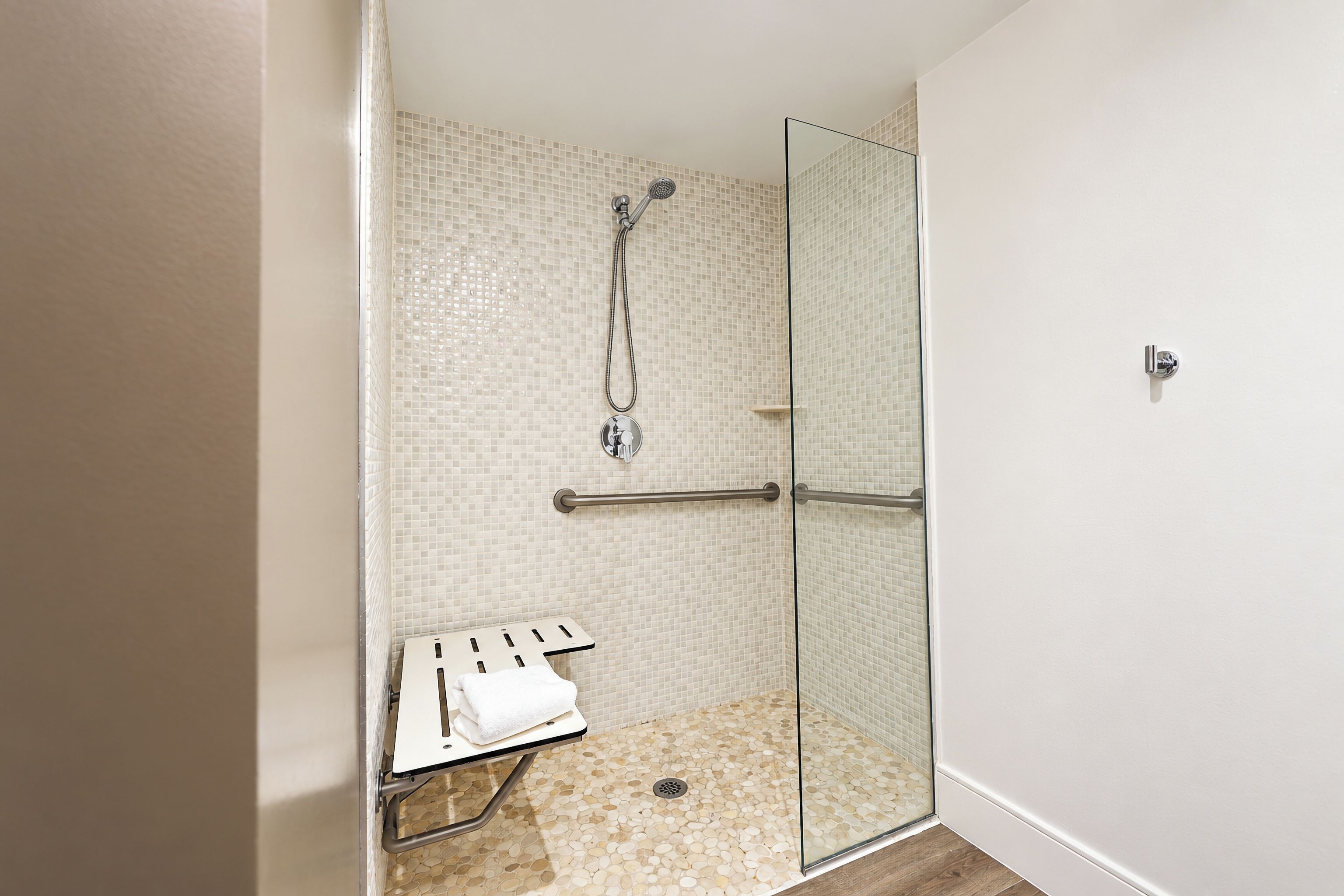 A glass-enclosed shower with a tiled wall and a small bench with a towel.