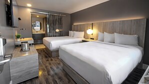 Moderni hotellihuone, jossa on kaksi sänkyä, työpöytä, peili ja suihkutila.