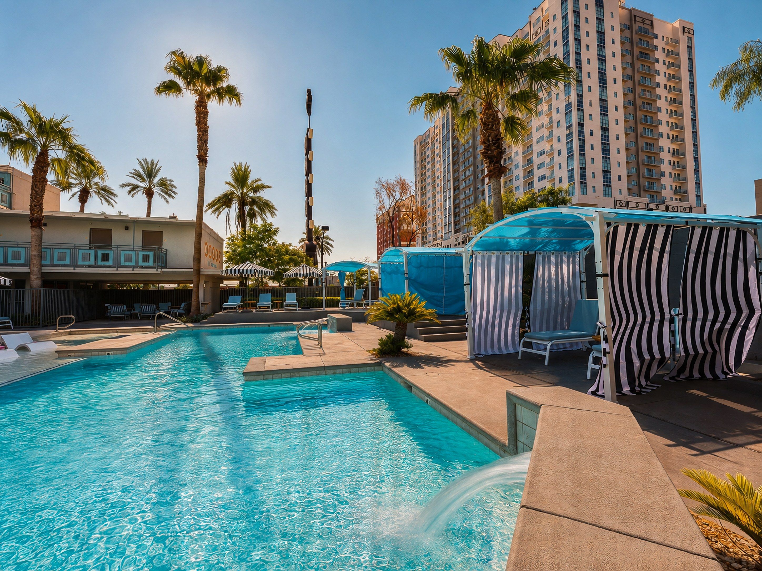 A swimming pool with lounge chairs and umbrellas, surrounded by palm trees and a high-rise building.