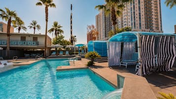 A swimming pool with lounge chairs and umbrellas, surrounded by palm trees and a high-rise building.