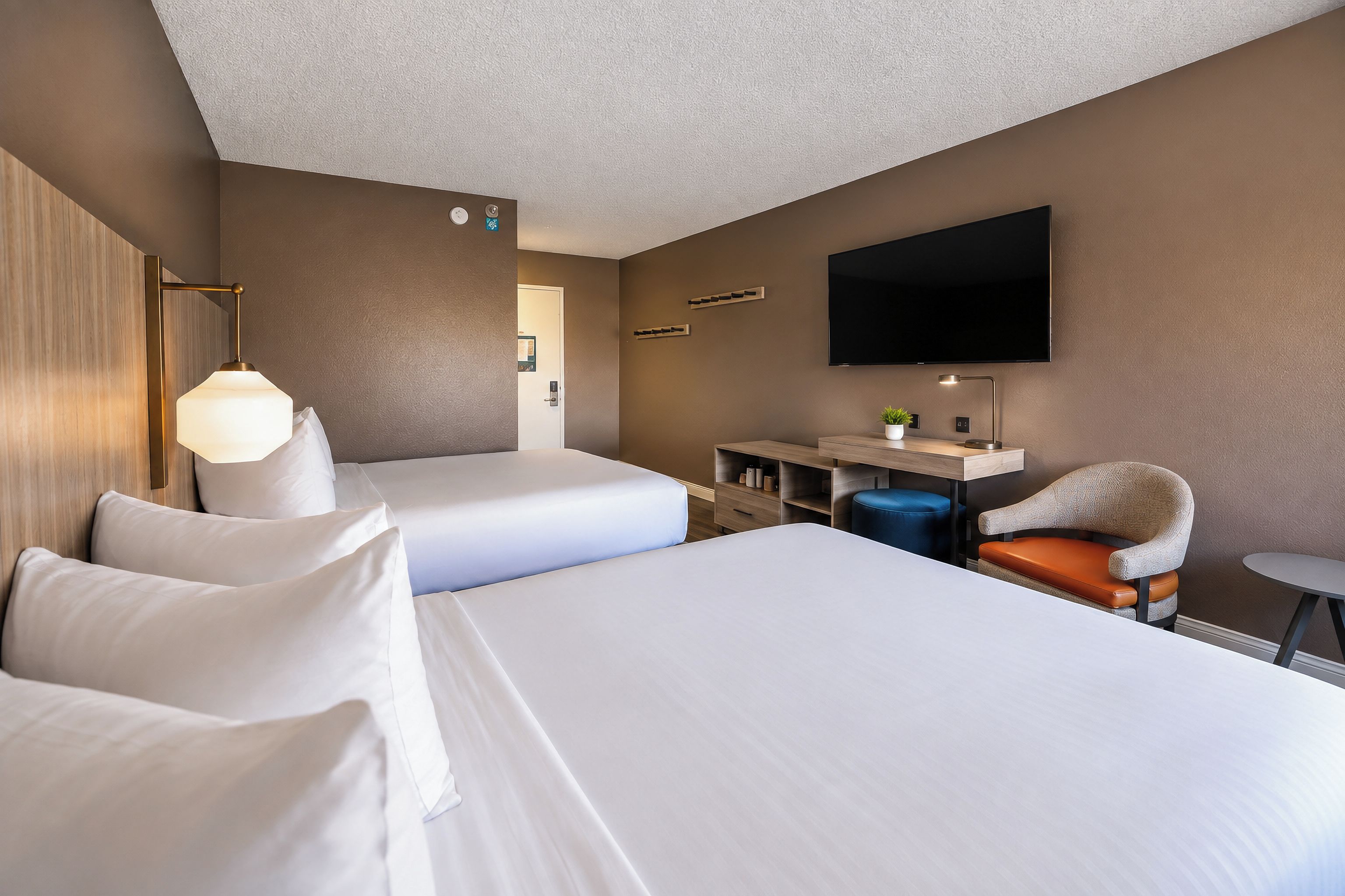 Habitació d'hotel amb dos llits, escriptori, cadira, televisió i làmpada.
