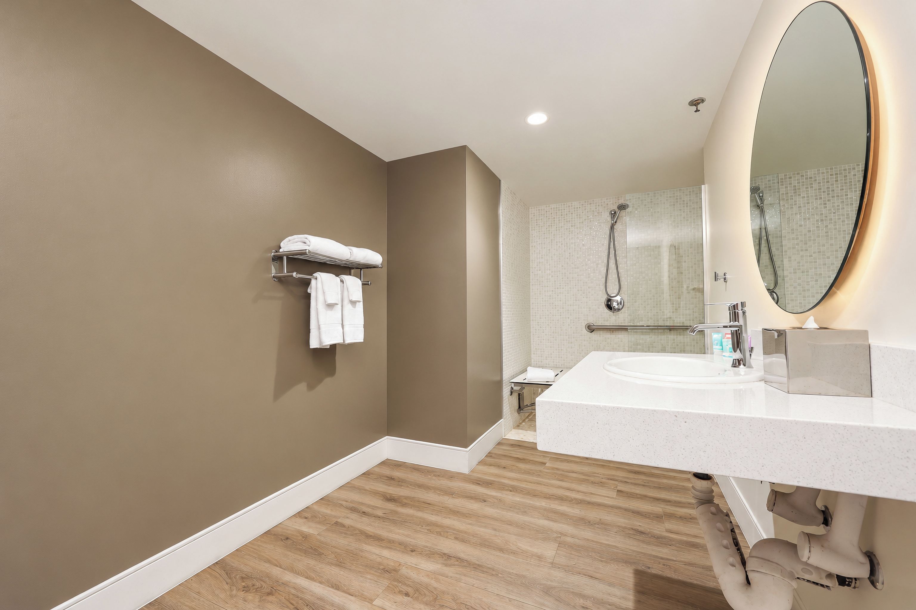 A modern bathroom with a wooden floor, a white sink, a large mirror, and a shower area.