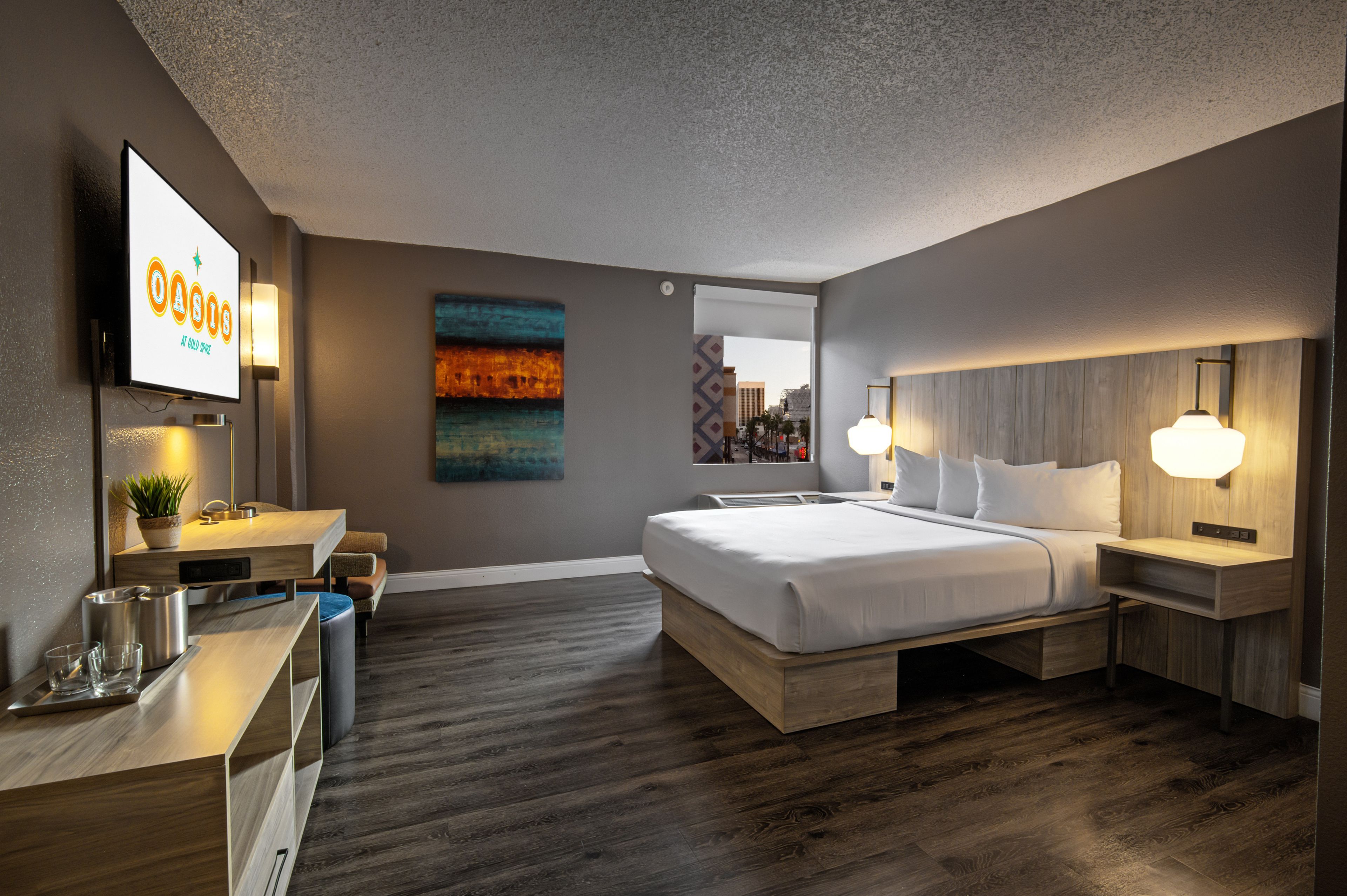 Habitación de hotel moderna con una cama grande, mesitas de noche, un escritorio con lámpara, televisor de pantalla plana y vistas a la ciudad.