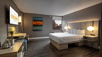 Habitación de hotel moderna con una cama grande, mesitas de noche, un escritorio con lámpara, televisor de pantalla plana y vistas a la ciudad.