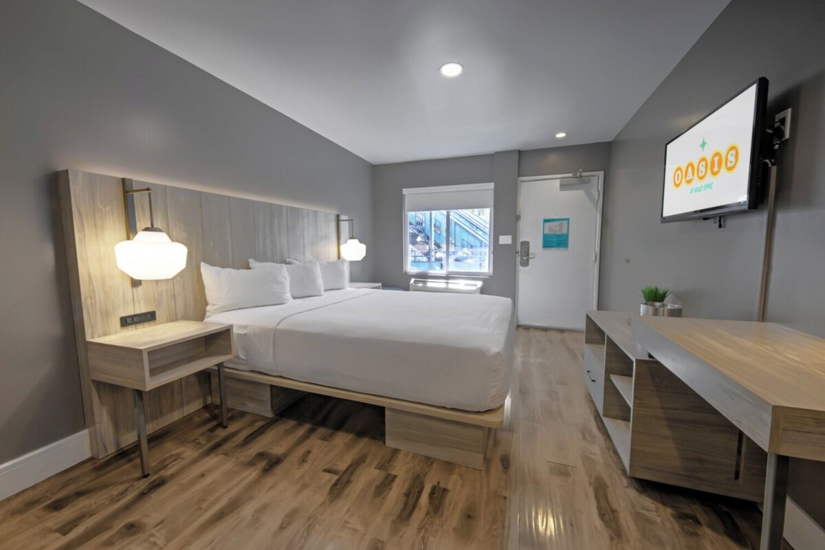 A modern hotel room with a large bed, bedside tables, a desk, and a TV on the wall.