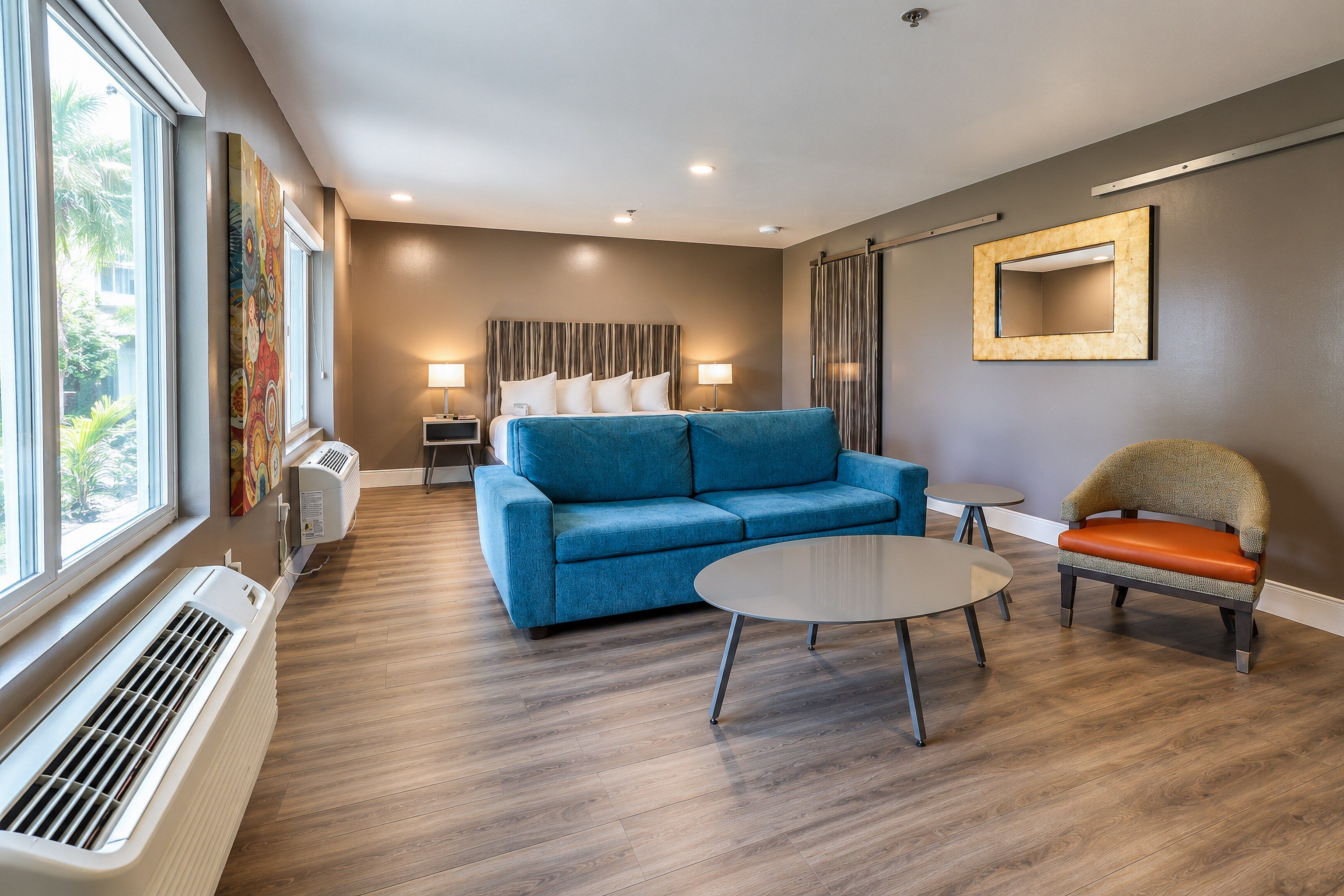 A modern hotel room with a blue sofa, a round table, and a chair with an orange cushion.