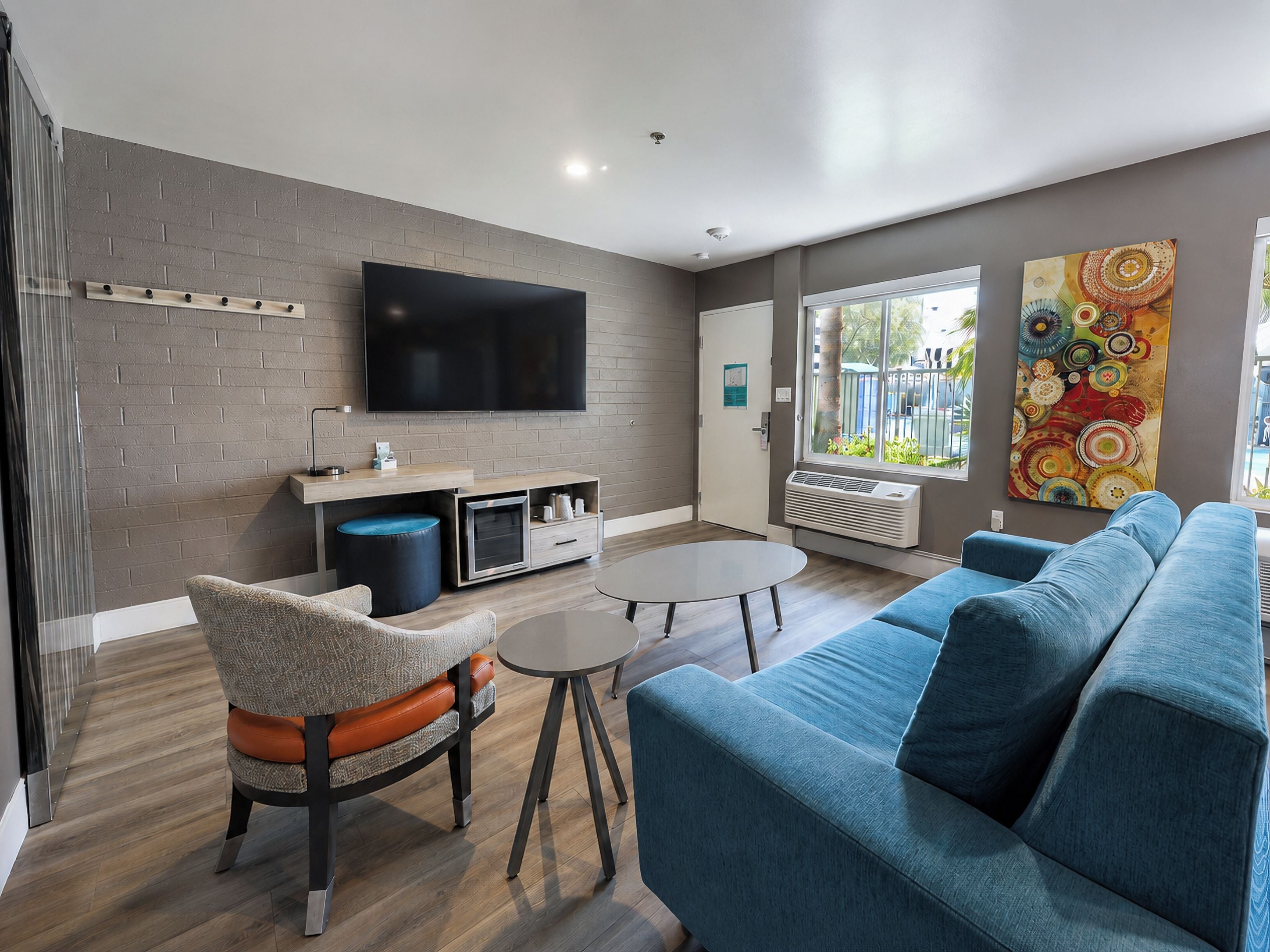 Een moderne woonkamer met een flatscreen televisie, een blauwe bank, een ronde salontafel en een muur met een bakstenen patroon.