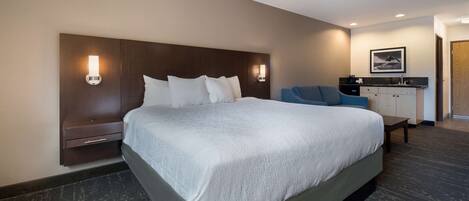 A hotel room with a large bed, a desk with a chair, and a small table.