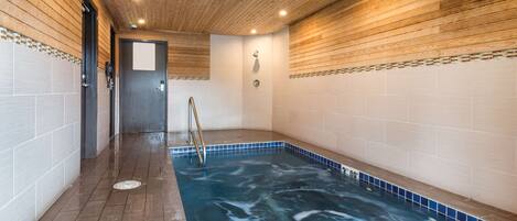 Uma área de spa com banheira de hidromassagem, teto de madeira, paredes azulejadas e uma escada de metal.