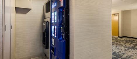 A hallway with a blue vending machine, a door, and a carpeted floor.