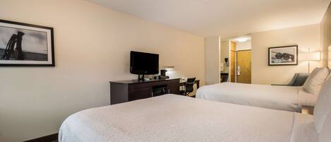 A hotel room with two beds, a desk, a television, and a framed picture on the wall.