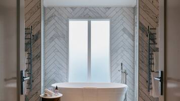 A modern bathroom with a herringbone-patterned wall, a freestanding bathtub, a small stool, and a towel rack.