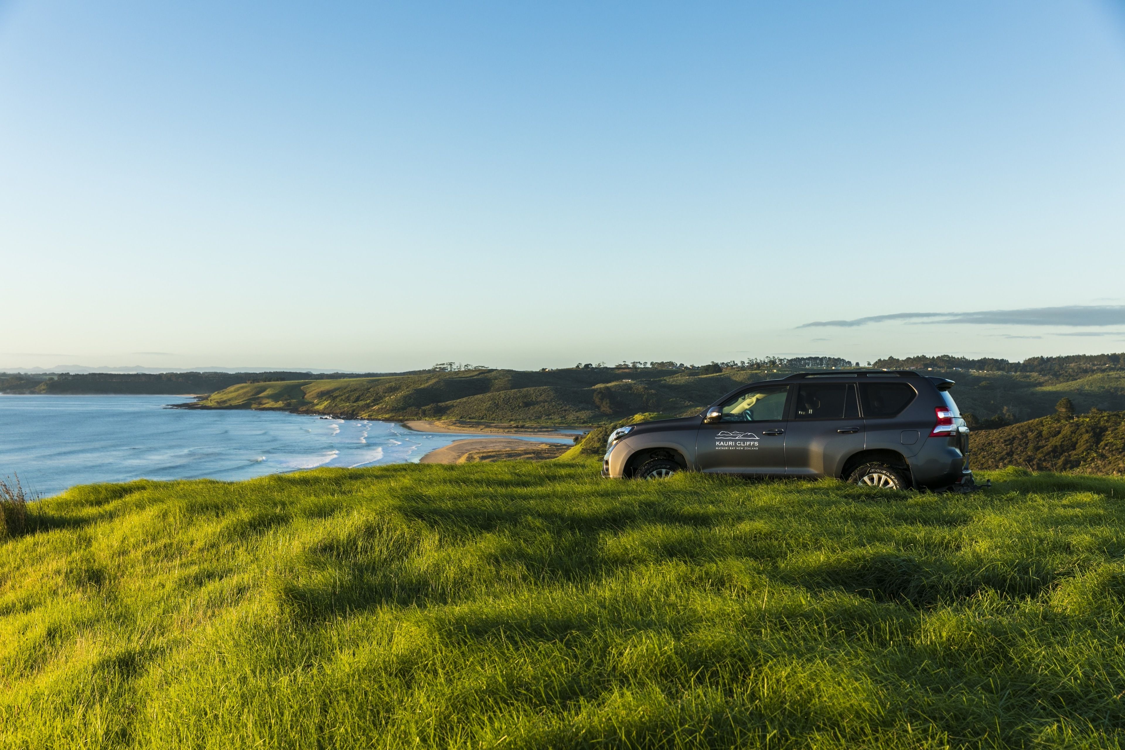 A vehicle parked on a grassy hill overlooking a coastal landscape.