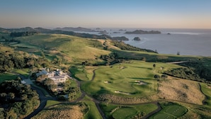 A golf course with a clubhouse, surrounded by rolling hills and a coastal view. - Rosewood Kauri Cliffs (Matauri Bay)