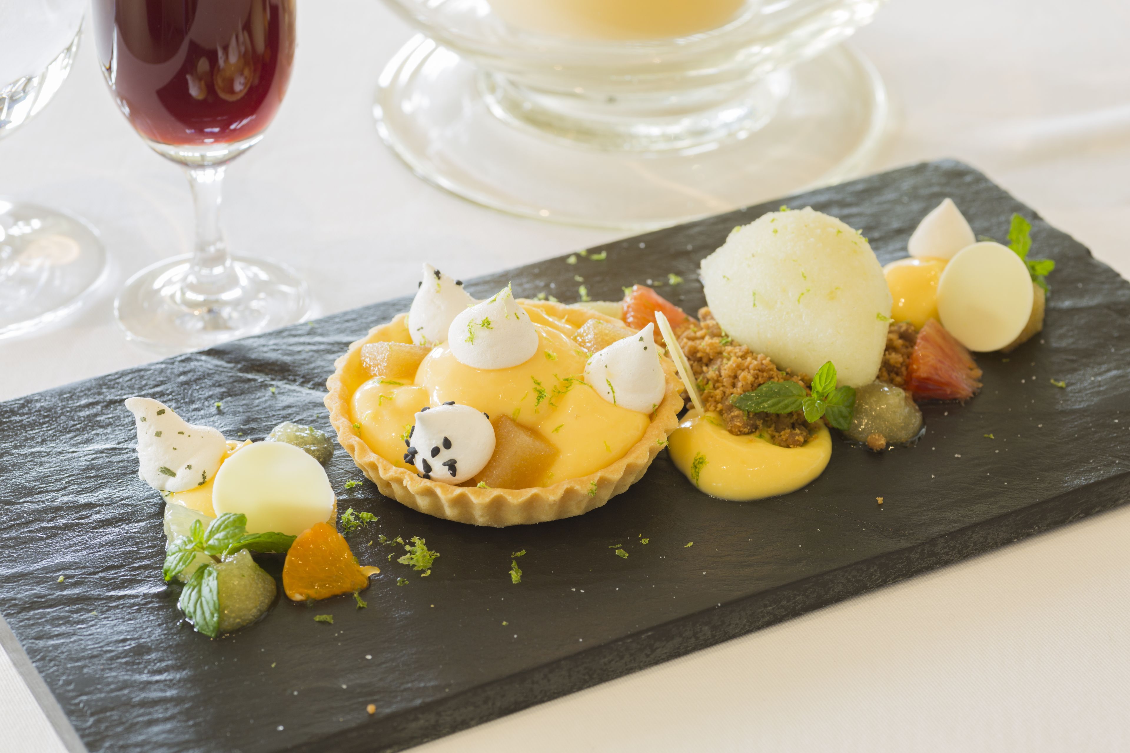 Une assiette à dessert avec une tarte, des fruits et une boule de glace, le tout présenté sur une ardoise.