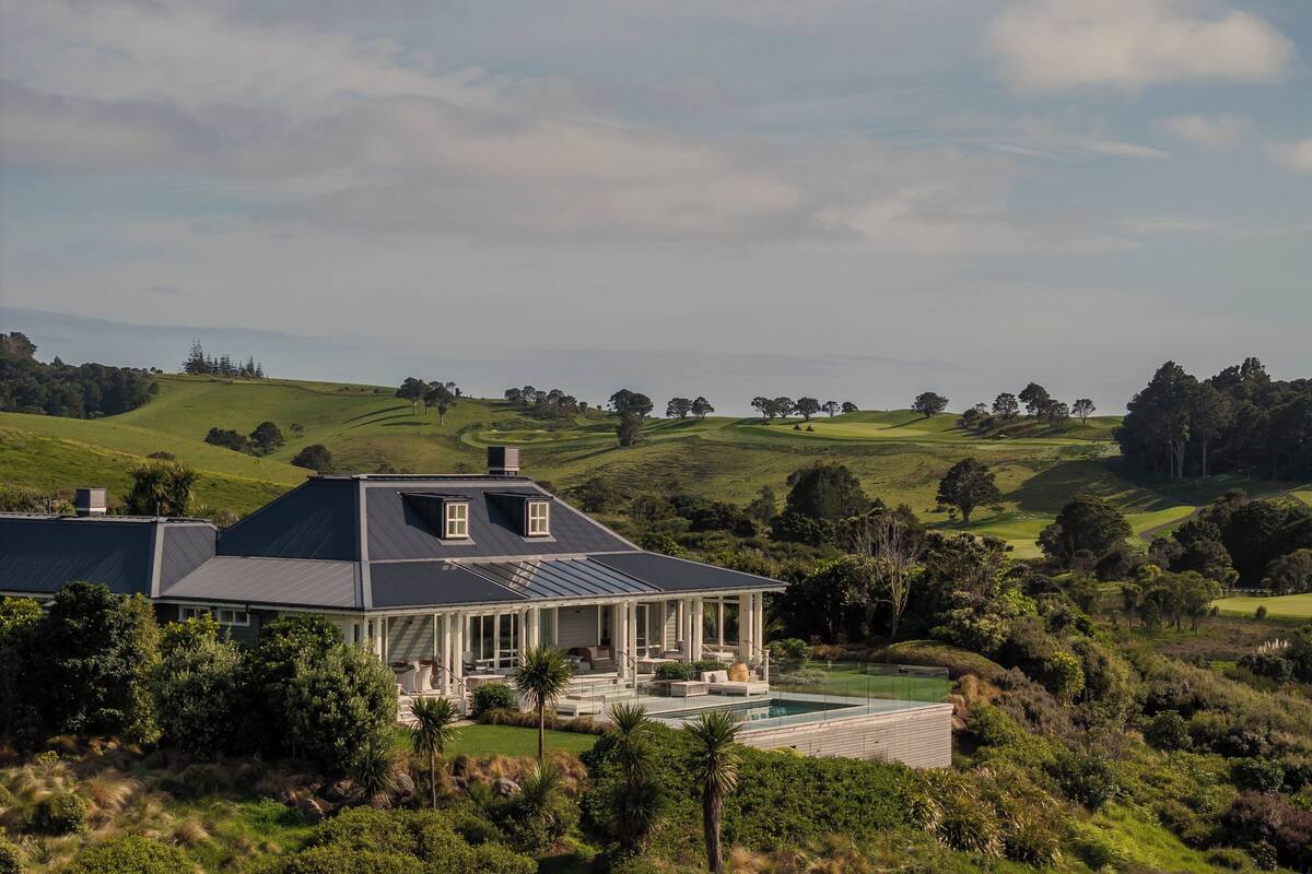 A large house with a swimming pool, surrounded by lush greenery and hills.