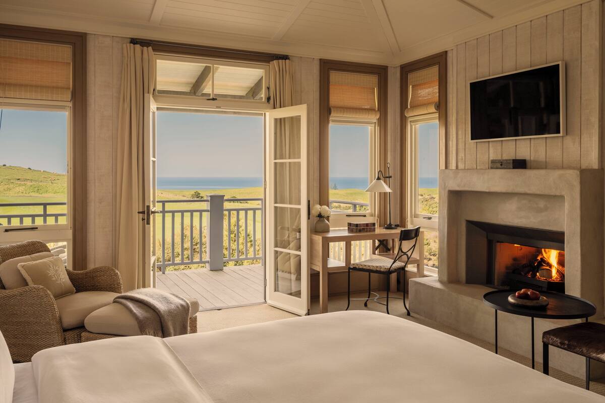A bedroom with a large bed, a desk with a chair, a television, and a fireplace.