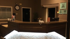 A hotel reception area with a modern design, including a reception desk, a clock, and a sign detailing office hours and check-in times. - Bay Hill Inns & Suites, Neepawa (Neepawa)