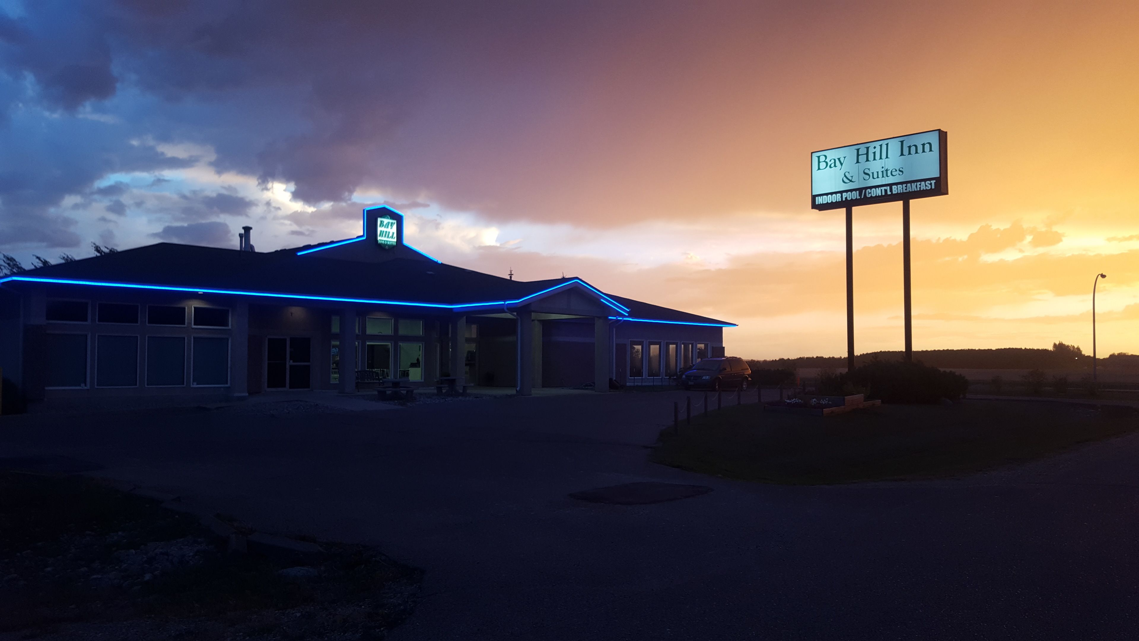 Un hôtel avec une enseigne indiquant « Bay Hill Inn & Suites » et proposant des équipements tels qu’une piscine intérieure et un petit-déjeuner continental.